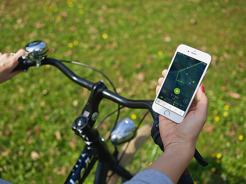 Auf dem Bild hät eine Person mit einer Hand sein Fahrrad fest und in der anderen Hand sein Telefon, auf dem eine Route abgebildet ist.