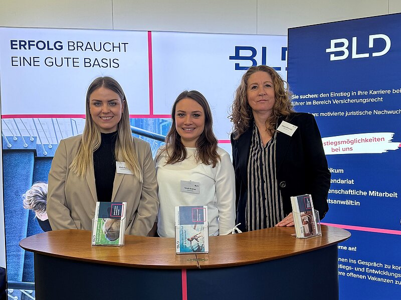 Das Bild entstand auf den Fakultätskarrieretag in Köln. Auf dem Foto stehen drei BLD Mitarbeiter am BLD Stand. Sie stehen hinter dem Podium und hinter Ihnen steht eine BLD LED Wand.