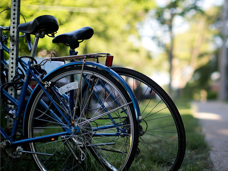 Es sind zwei Fahrräder an einem Pfosten an einen Fußgängerweg mit grünem Rasen.angekettet.